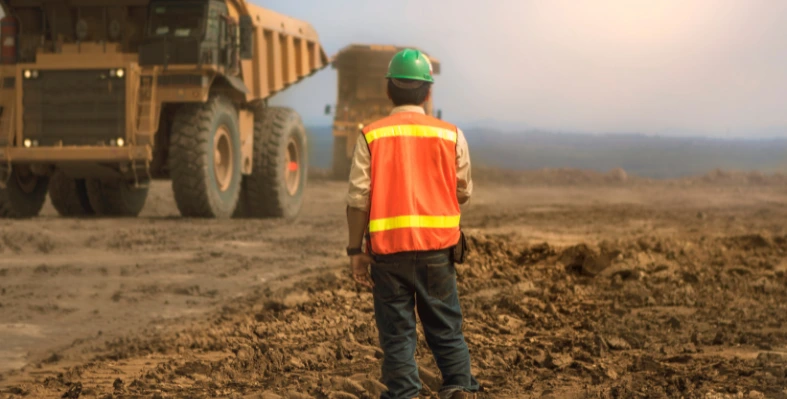 A_worker_in_high_visibility_gear_observing_large_haul_trucks